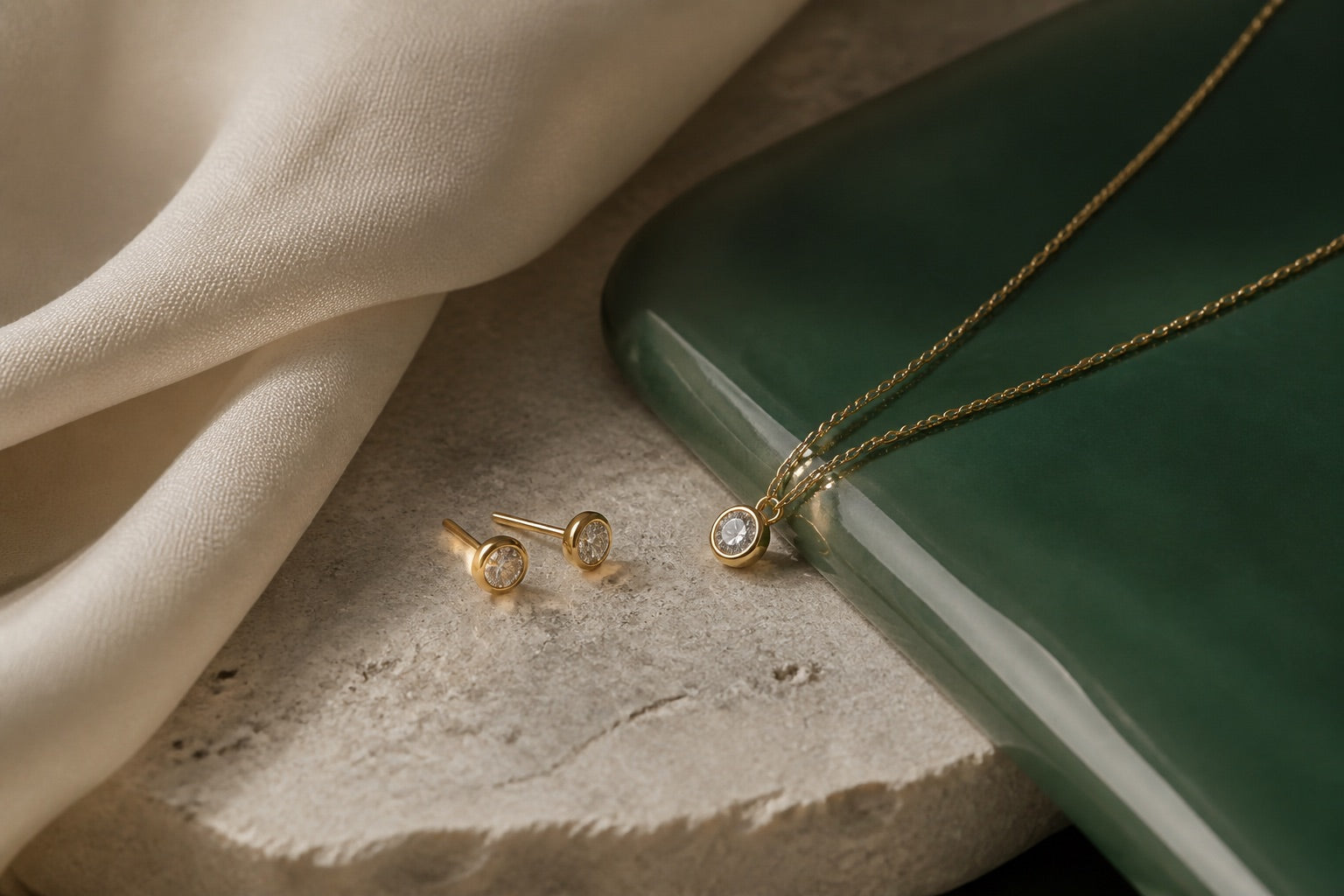 Gold jewellery arranged on oyster stone, cream silk, and prestige green